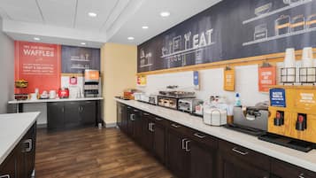 Une cuisine moderne avec des meubles en bois foncé, un plan de travail blanc et divers appareils, comme un appareil à gaufres et une machine à café.
