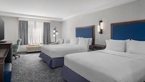 Une chambre d’hôtel avec deux lits, un bureau, une chaise, une télévision et une fenêtre avec des rideaux.