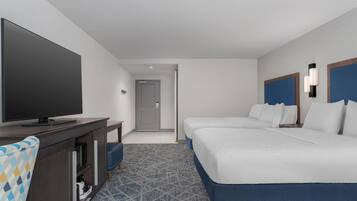 A hotel room with a flat-screen TV, a desk with a microwave, two beds with blue headboards, and a patterned carpet.