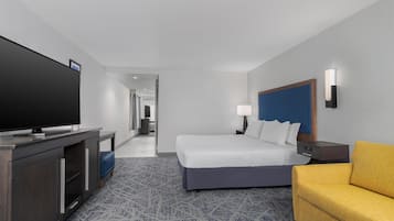 A hotel room with a bed, a television on a desk, a sofa, and a lamp.