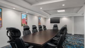 A conference room with a long table, black leather chairs, a flat-screen TV, and framed artwork on the walls.