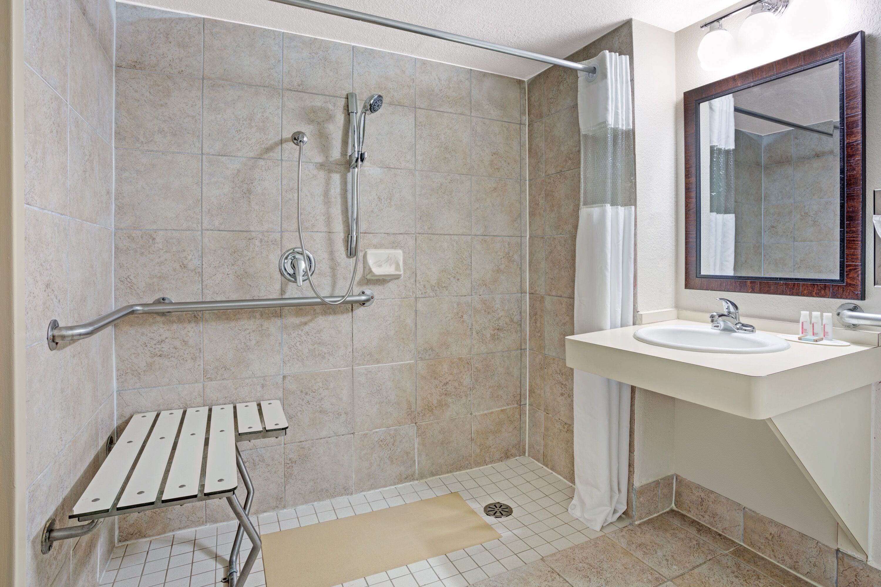 Een badkamer met een douche, wastafel, spiegel en een handgreep.