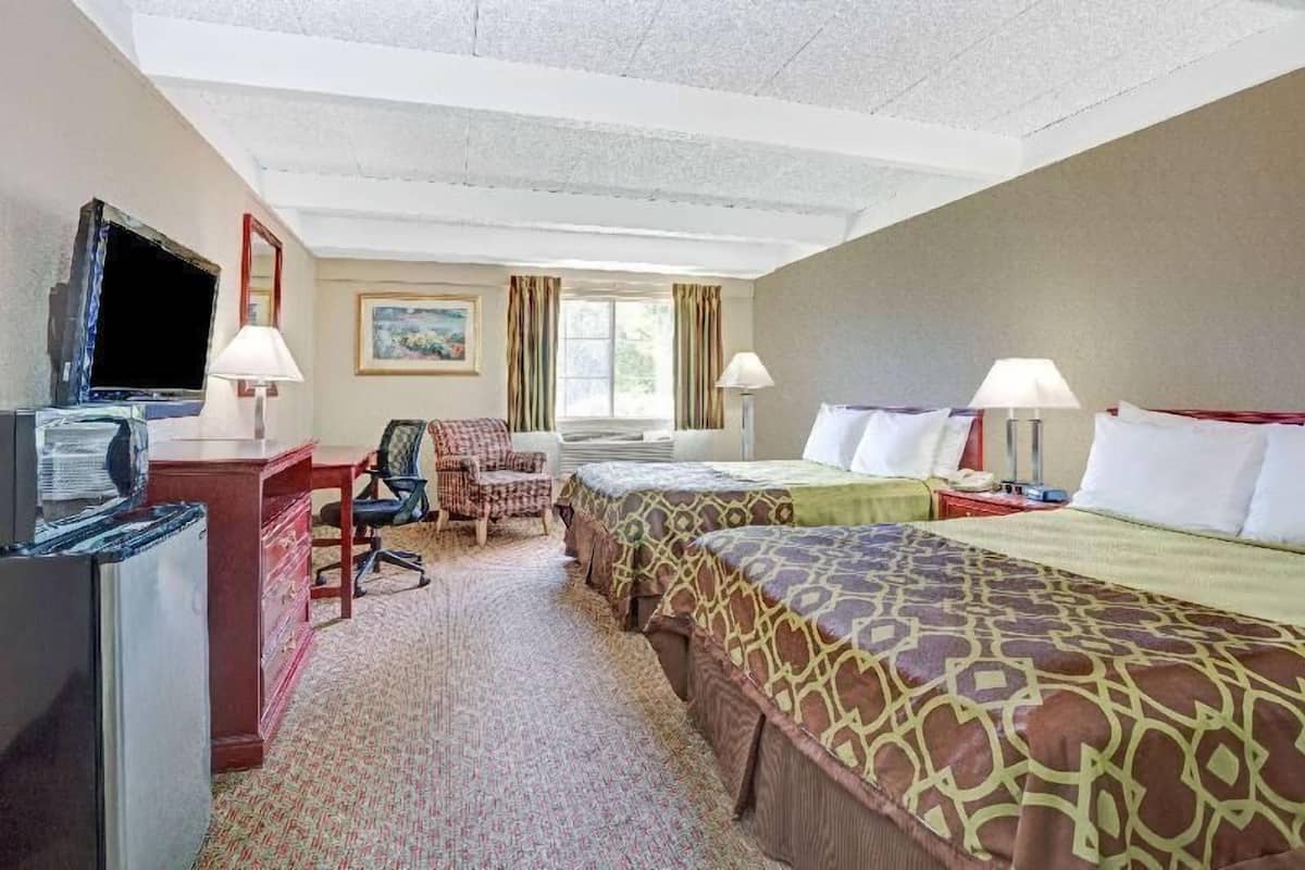 A hotel room with a desk, chair, two beds, a TV, and a window.