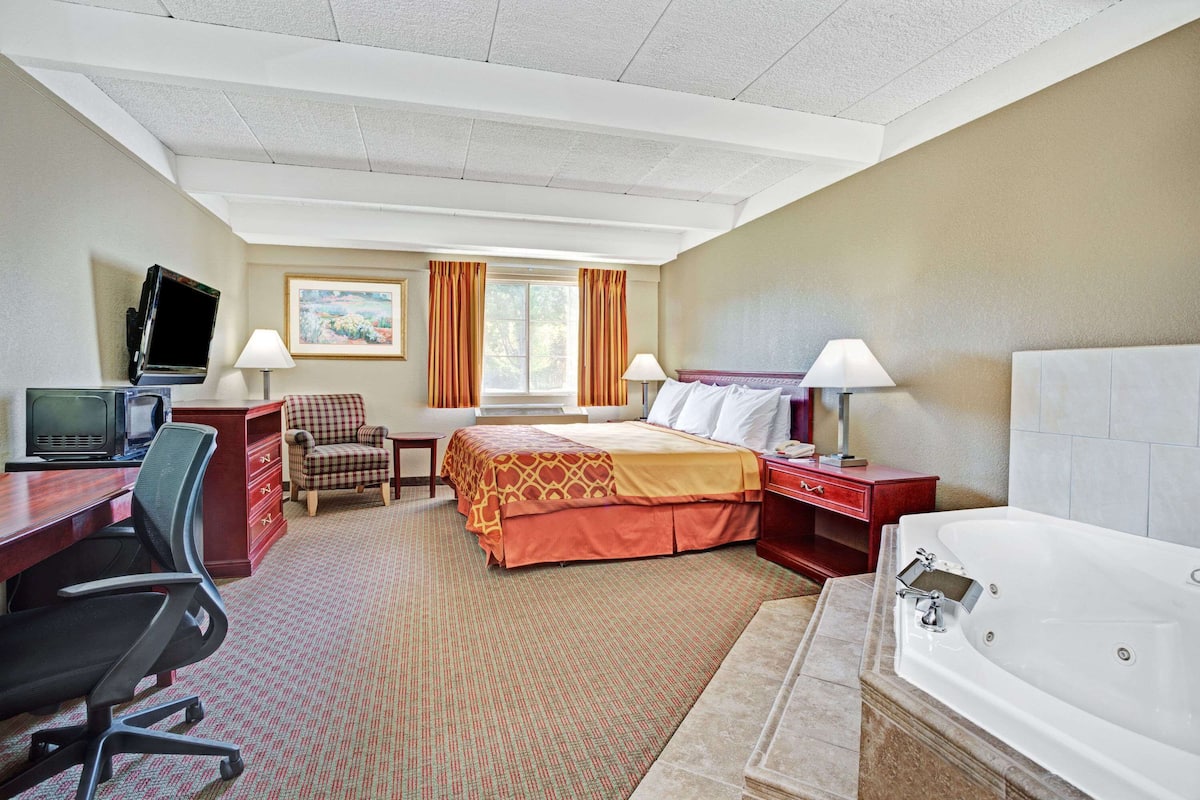 A hotel room with a bed, desk, chair, TV, and a bathtub.