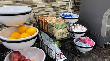 A kitchen counter with various bowls containing fruits and packaged goods, a coffee maker, and a tiled backsplash.