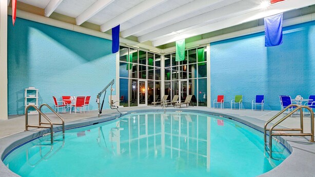 Una piscina interior con agua azul cristalina, rodeada de sillones de descanso y un área acristalada con vistas a la ciudad.