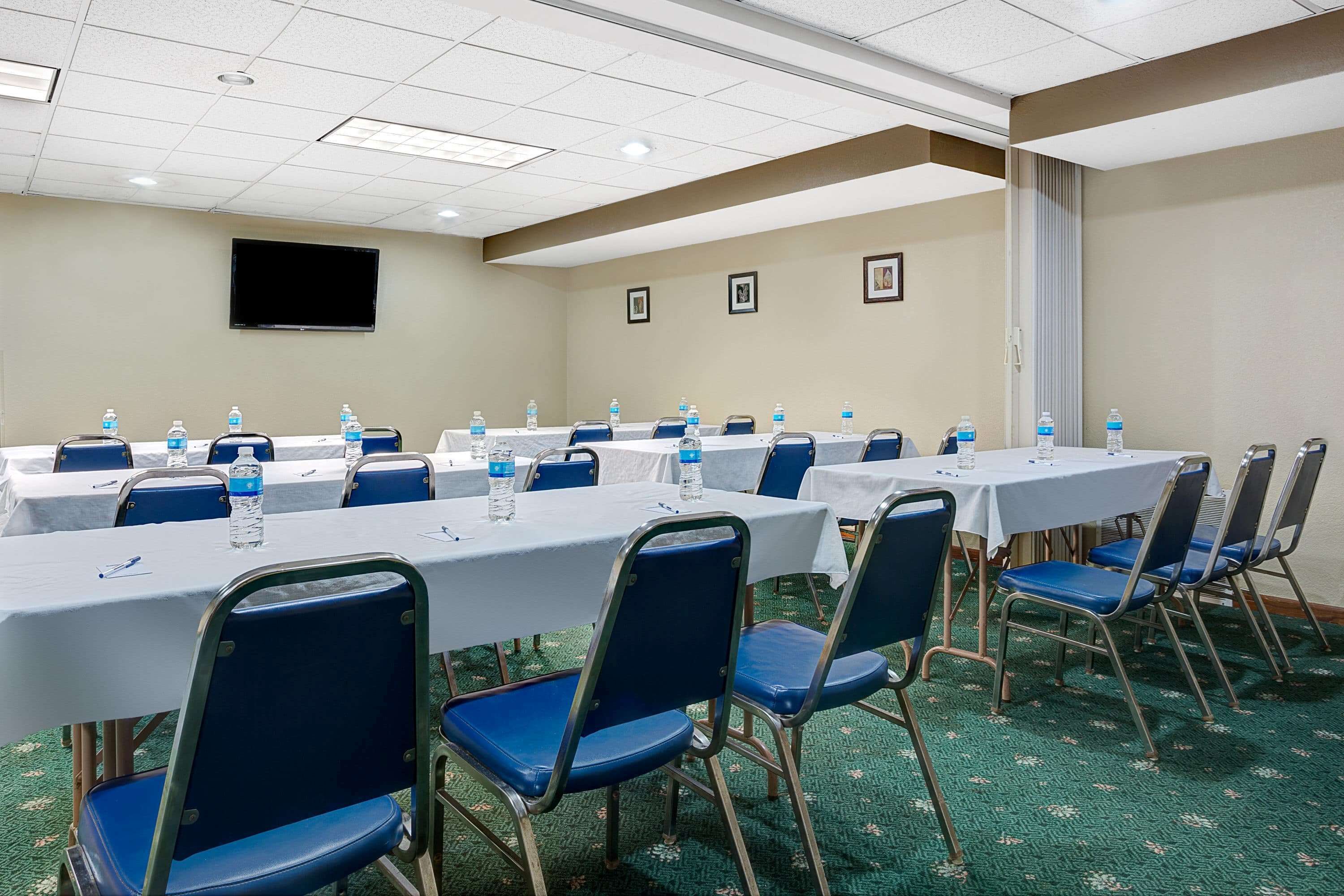 A conference room with multiple tables and chairs, water bottles, and a flat-screen TV on the wall.