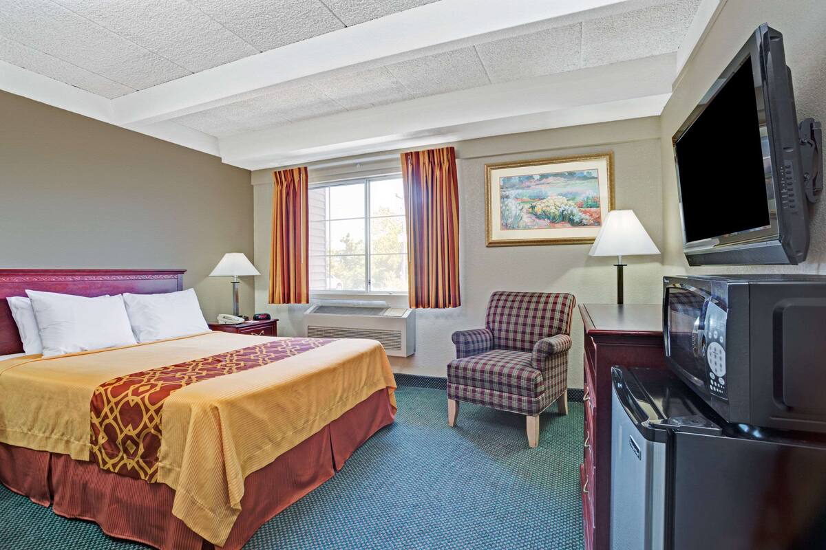 A hotel room with a bed, a chair, a TV, a lamp, and a painting on the wall.