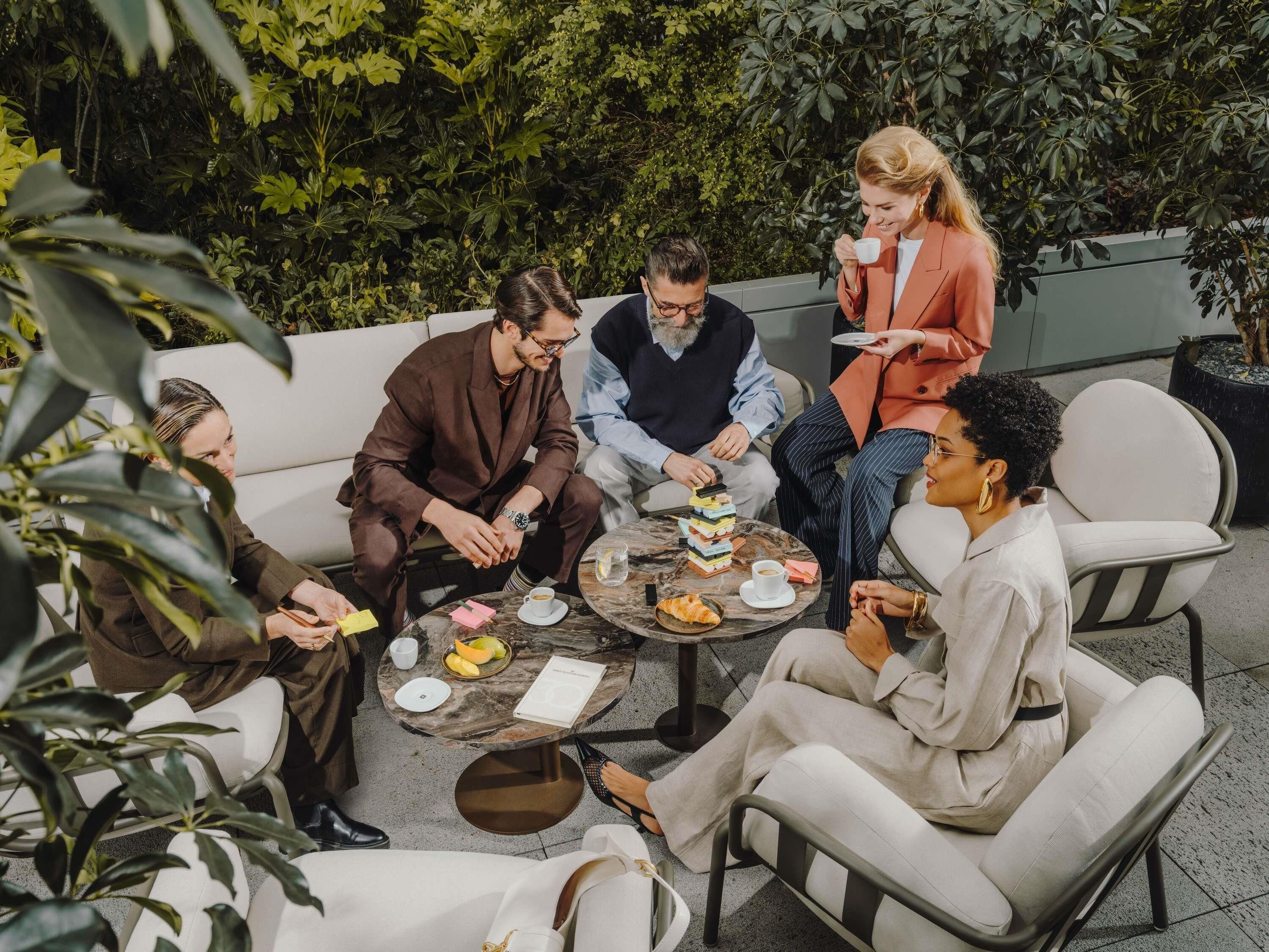 Un grupo de personas sentadas alrededor de una mesa al aire libre, conversando.