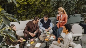 Un grupo de personas sentadas alrededor de una mesa al aire libre, conversando.