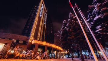 Un edificio alto con ventanas iluminadas y el suelo cubierto de nieve.