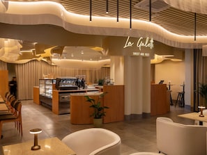 L’intérieur d’un café moderne, avec un comptoir central, un espace salon et une enseigne indiquant « La Galerie SWEET AND MEET ».