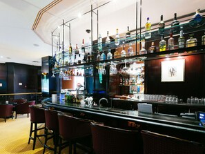 A bar area with a curved counter, multiple stools, and a variety of liquor bottles. - Pullman Bucharest (Bucharest)