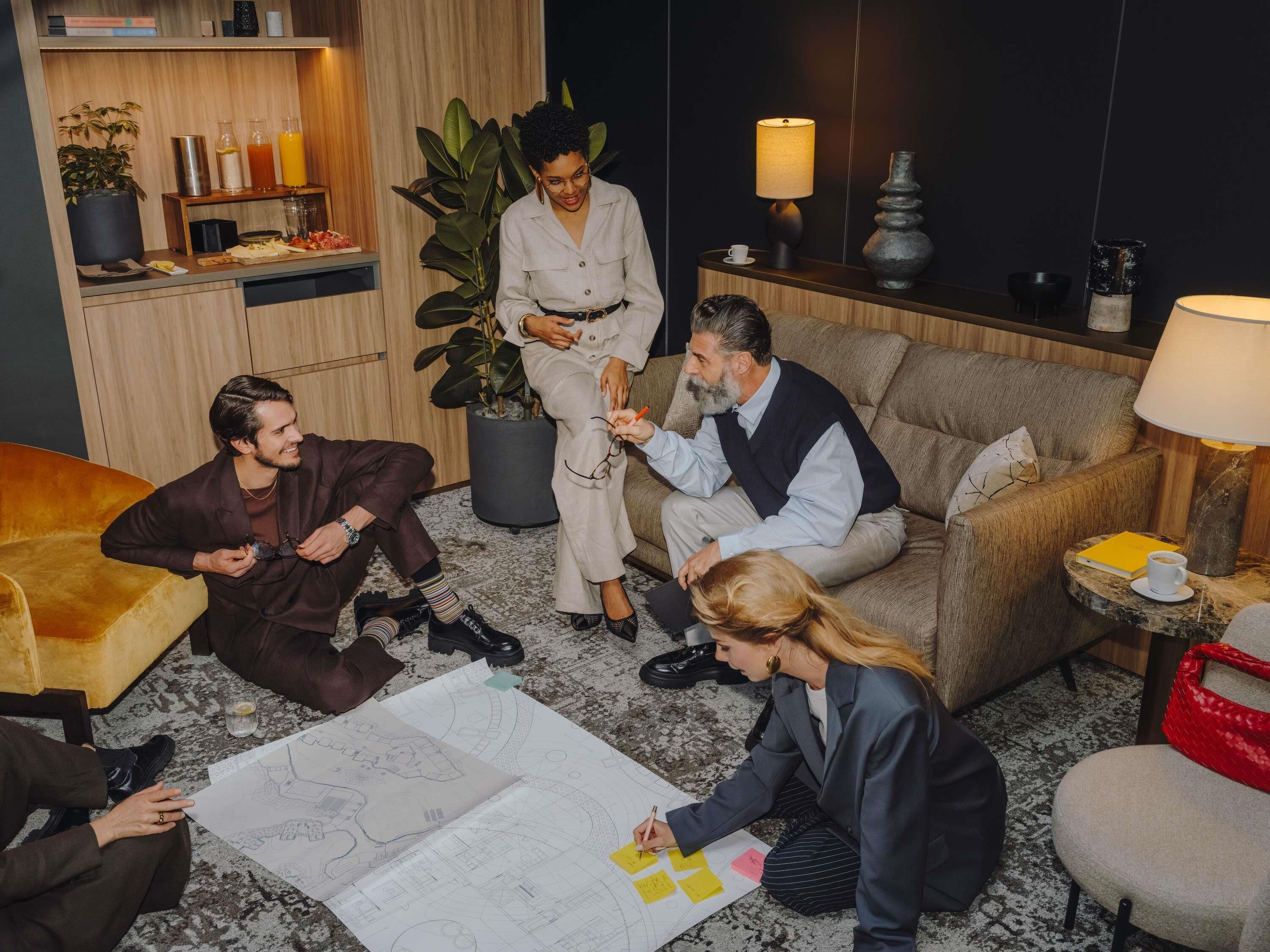 A group of people in a room with a wooden floor, a sofa, a coffee table, and a bookshelf with books and decorative items.
