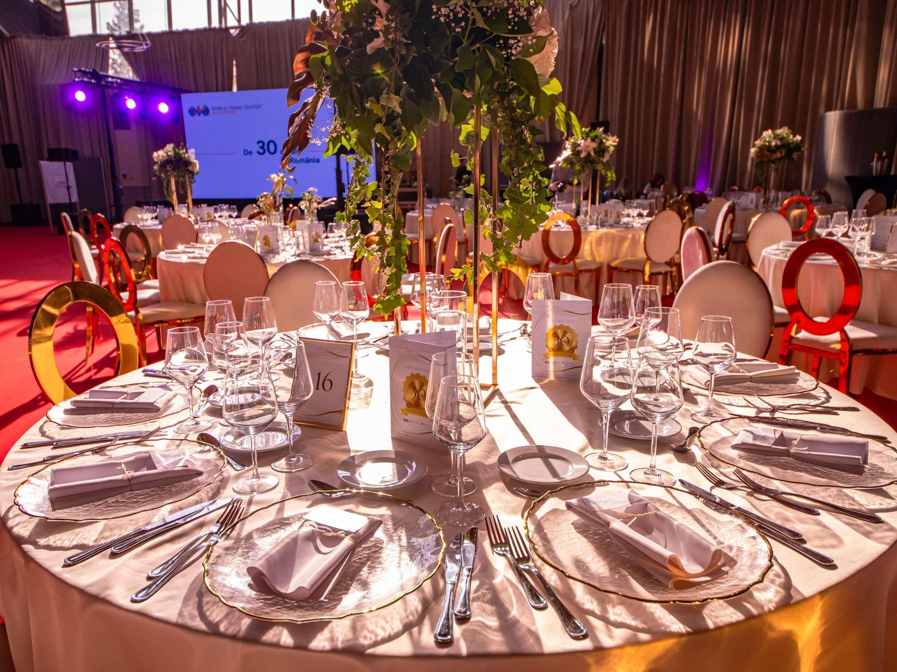 Un salón de banquetes con mesas redondas dispuestas para un evento formal, con vajilla y centros de mesa florales.