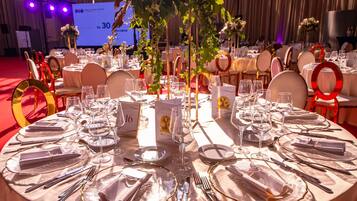 Un salón de banquetes con mesas redondas dispuestas para un evento formal, con vajilla y centros de mesa florales.