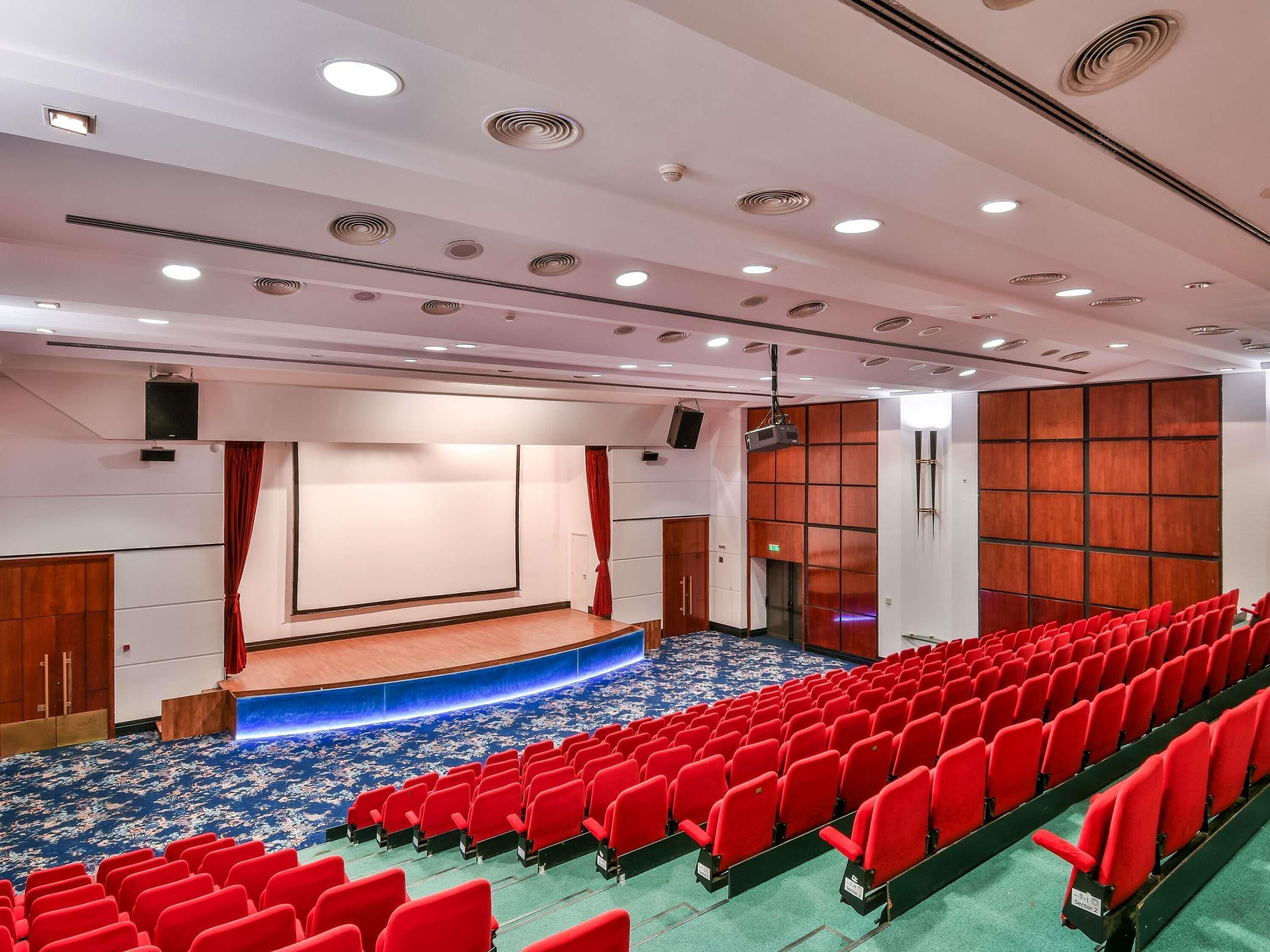 A theater with a stage, red seating, and a blue carpet.
