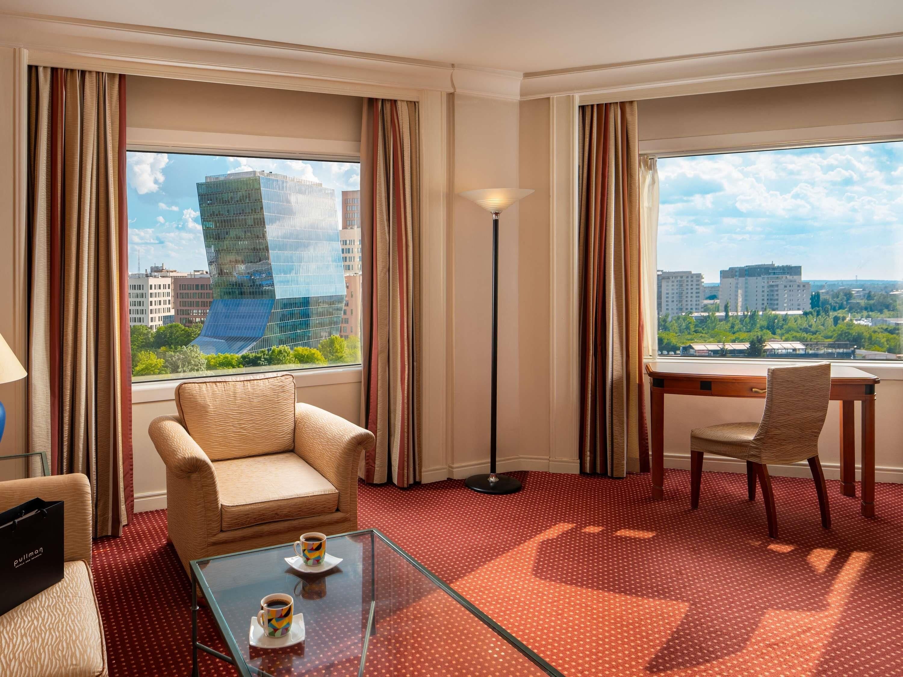 Habitación de hotel con sofá, sillón y una mesa de centro de cristal con dos tazas.