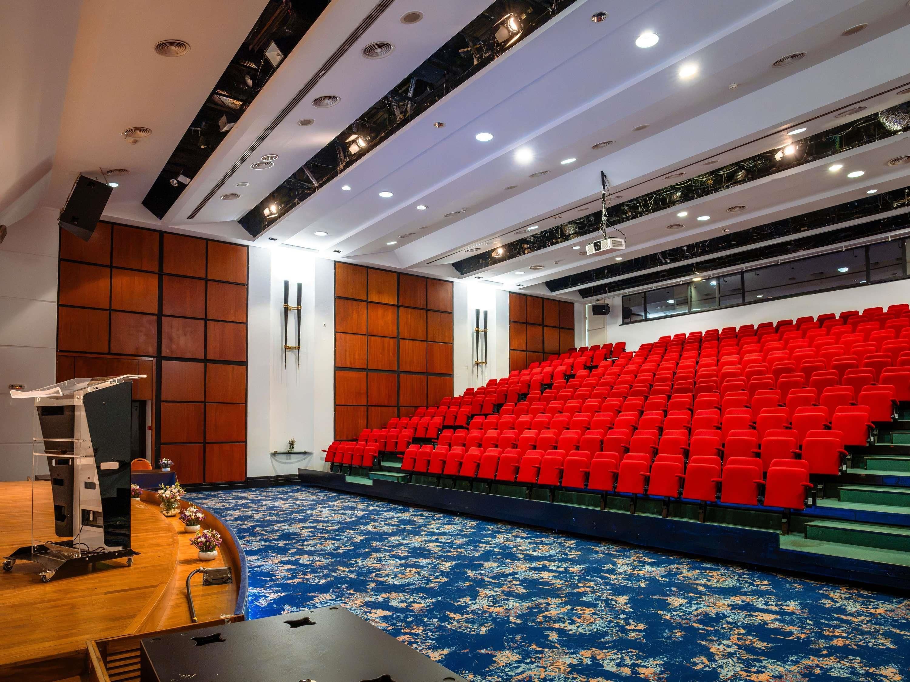 Ein Theater mit Bühne, roten Sitzplätzen und einem blau gemusterten Teppich.