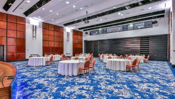 A large conference room with round tables, orange chairs, and a blue patterned carpet.