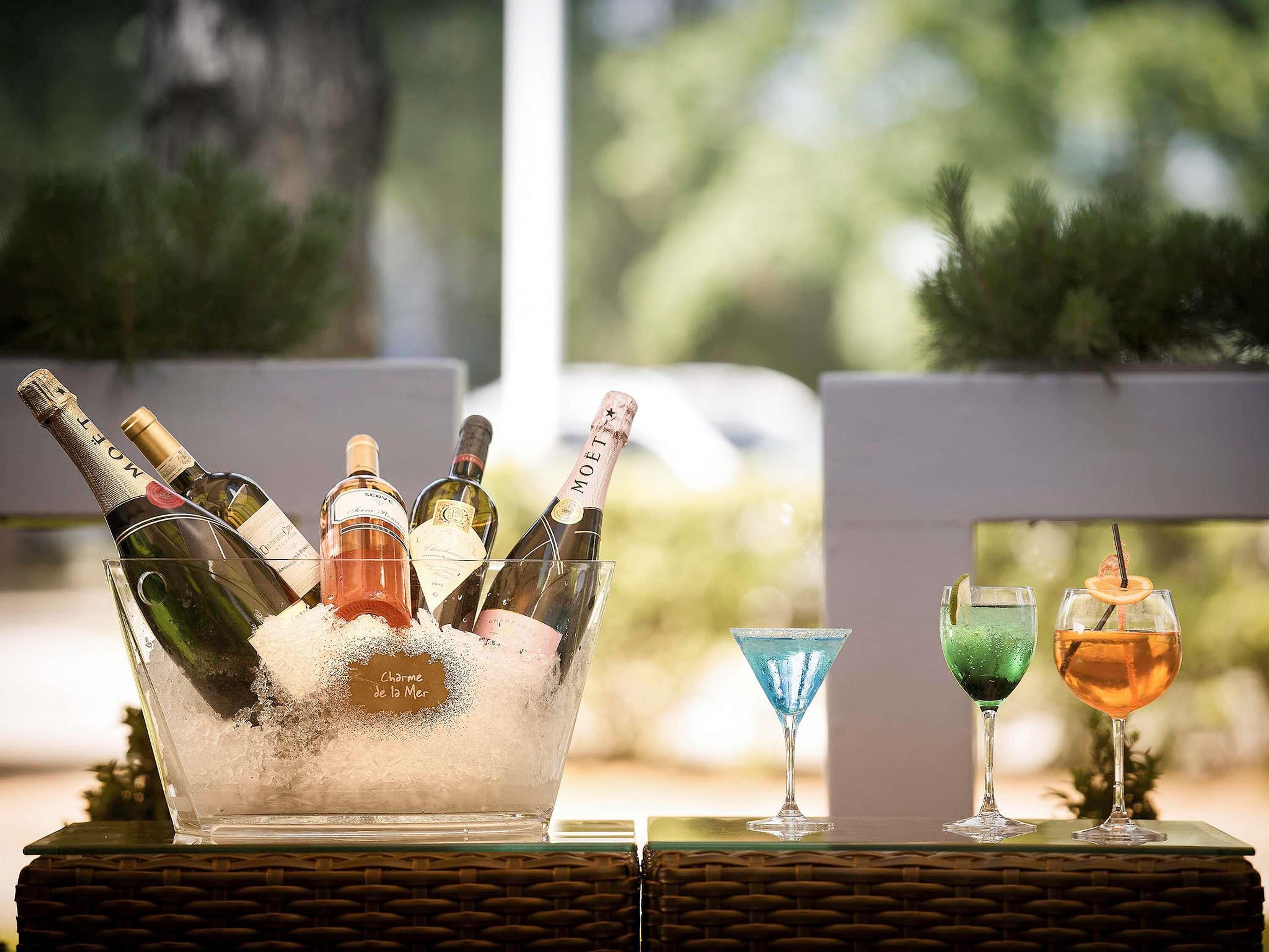 A table with a bottle of Moët champagne, a bottle of rosé wine, and a bottle of white wine in a glass bowl filled with ice. There are also two cocktail glasses with different colored drinks.