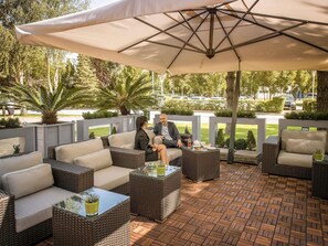 An outdoor seating area with wicker furniture and a large umbrella. - Pullman Bucharest (Bucharest)