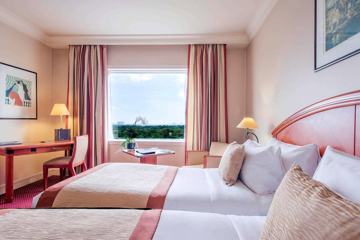 A hotel room with a large bed, a desk, a chair, a small table, and a window with curtains.