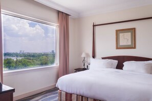 A hotel room with a large window, a bed, a nightstand, a lamp, and a framed picture on the wall.