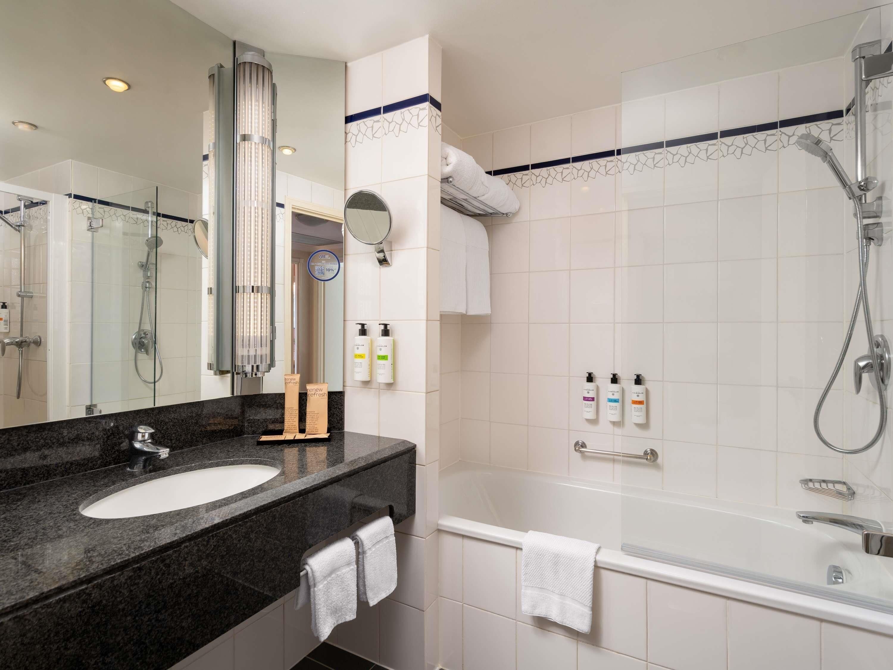A modern bathroom with a sink, mirror, shower, and toiletries.