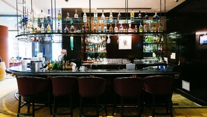 A bar area with multiple shelves of liquor bottles, a bar counter, and four bar stools. - Pullman Bucharest (Bucharest)