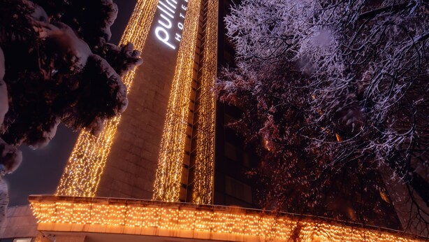 A hotel with a prominent vertical sign, large windows, and a snow-covered ground. - Pullman Bucharest (Bucharest)