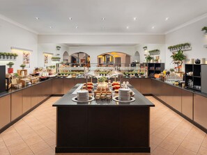 A modern buffet setup with a central island, glass display cases, and various food items. - Pullman Bucharest (Bucharest)