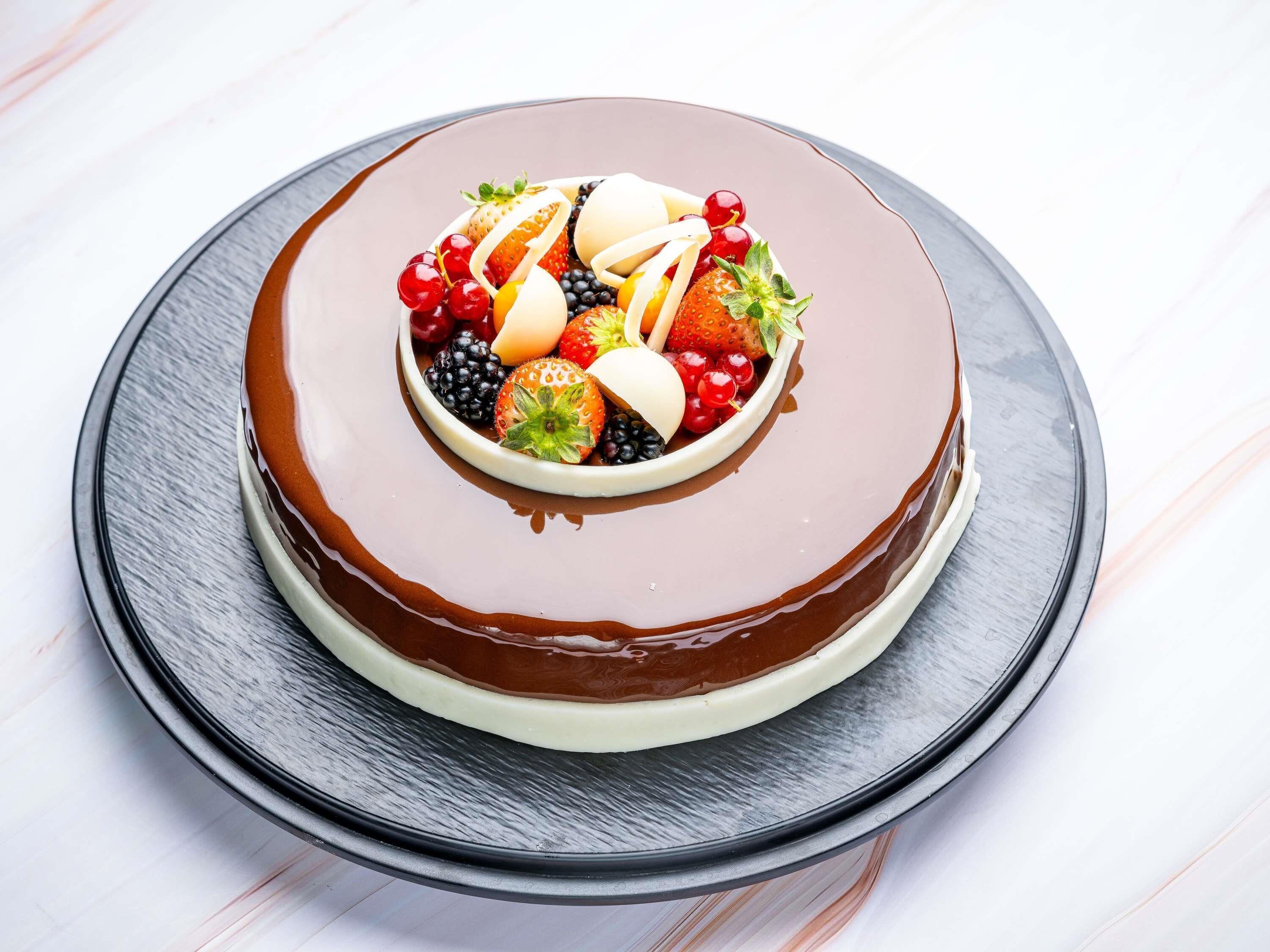 Un pastel redondo cubierto de chocolate y decorado con frutas sobre un plato.