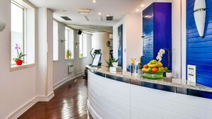 A hotel reception area with a curved white reception desk, a blue wall with a decorative light fixture, and a window with a potted plant. - Pullman Bucharest (Bucharest)