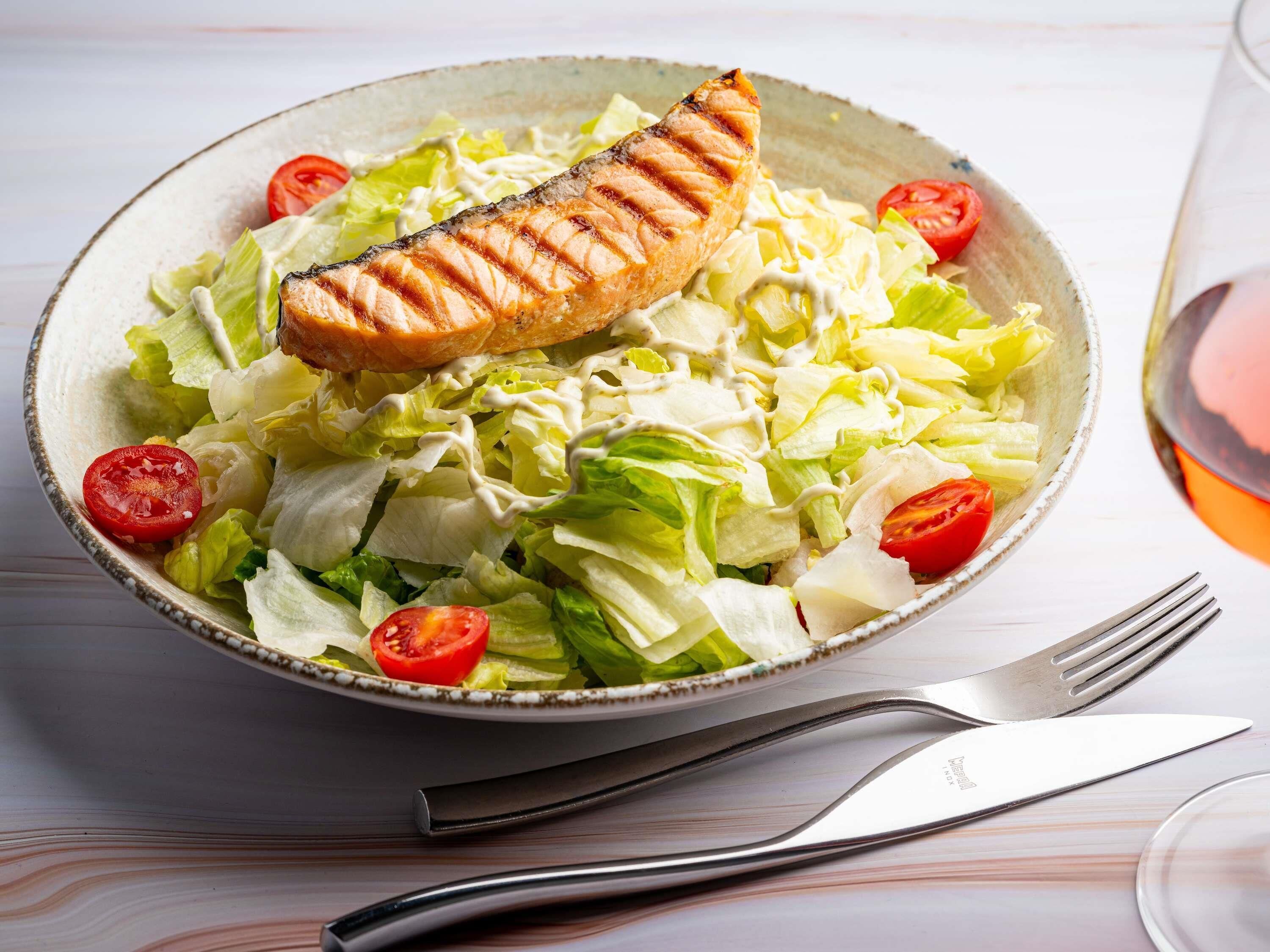 A bowl of salad with grilled salmon and cherry tomatoes.