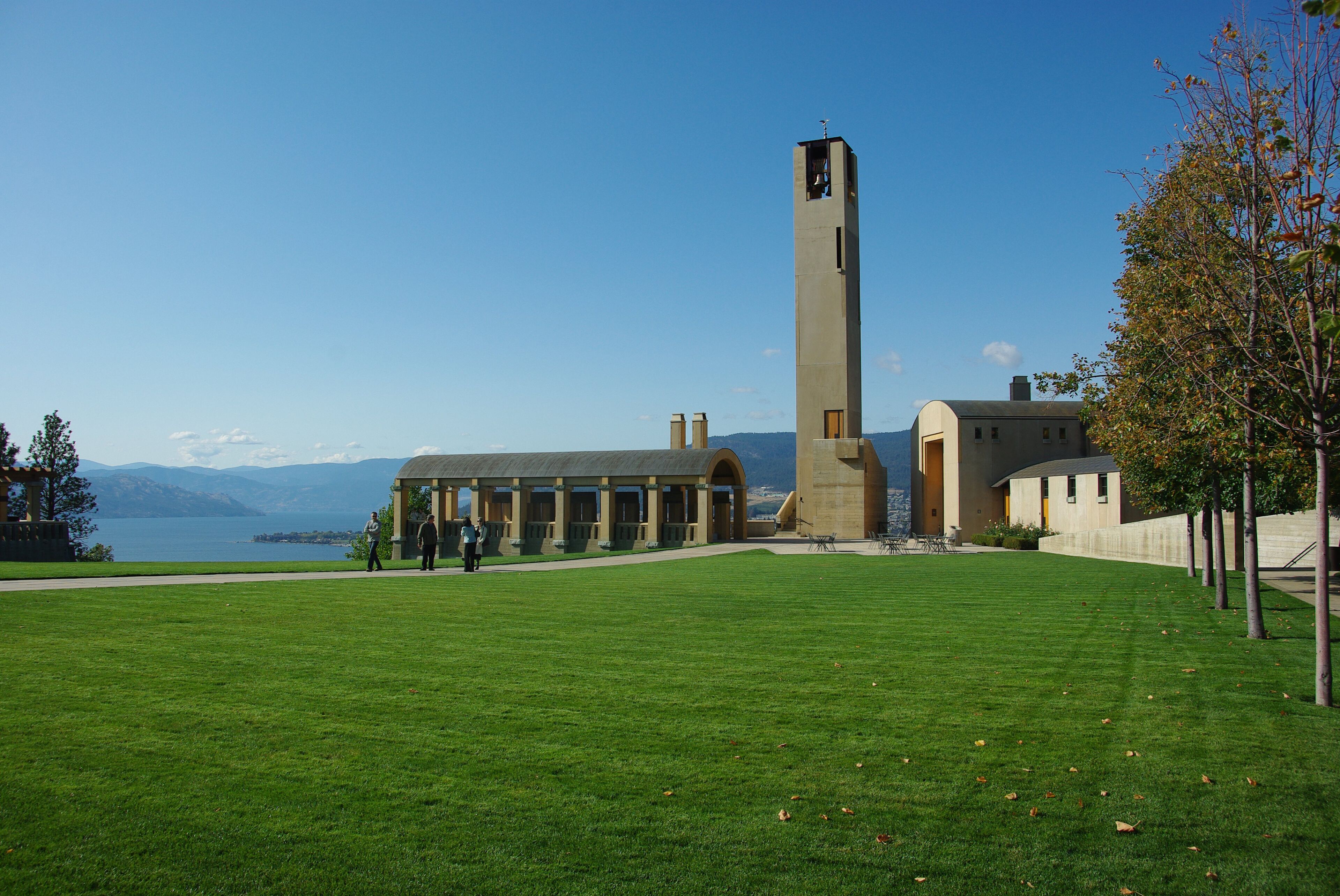 Ein Gebäude mit einem hohen Turm, einer Rasenfläche und einem Gewässer im Hintergrund.