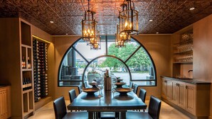 A dining area with a large table set for six, a wine rack, and a view through a large window.