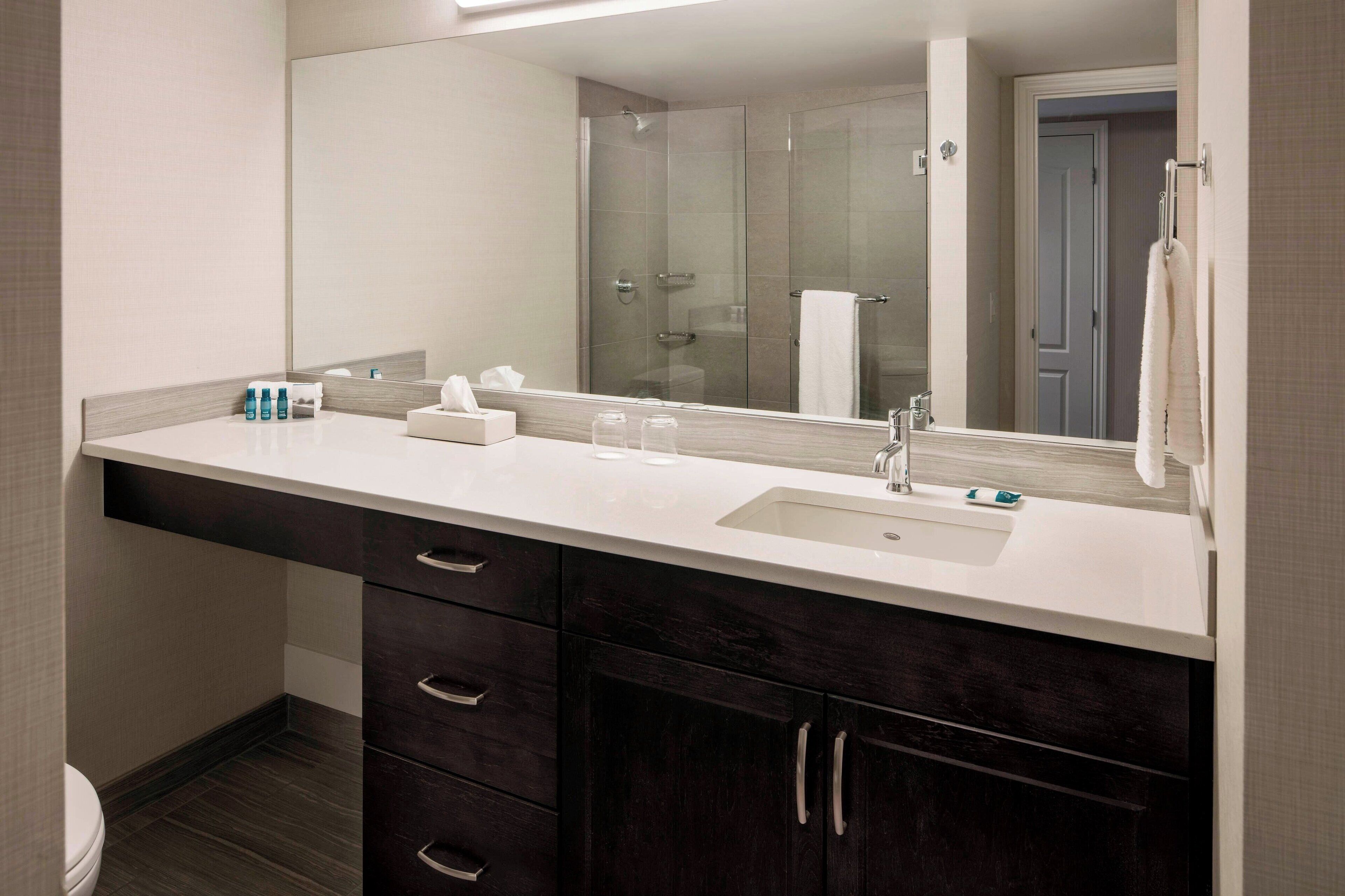 A modern bathroom with a large mirror, a sink, dark wooden cabinets, and a glass shower enclosure.