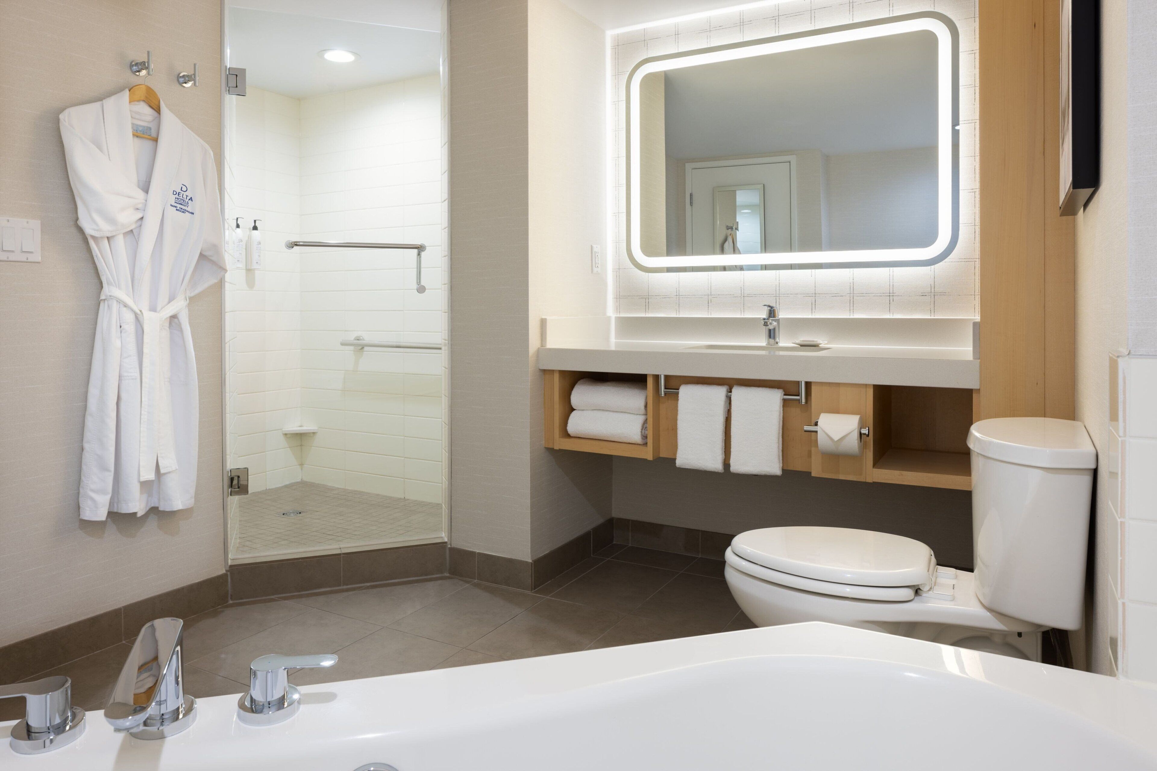 A modern bathroom with a glass-enclosed shower, a white bathtub, a sink with a mirror, and a toilet.