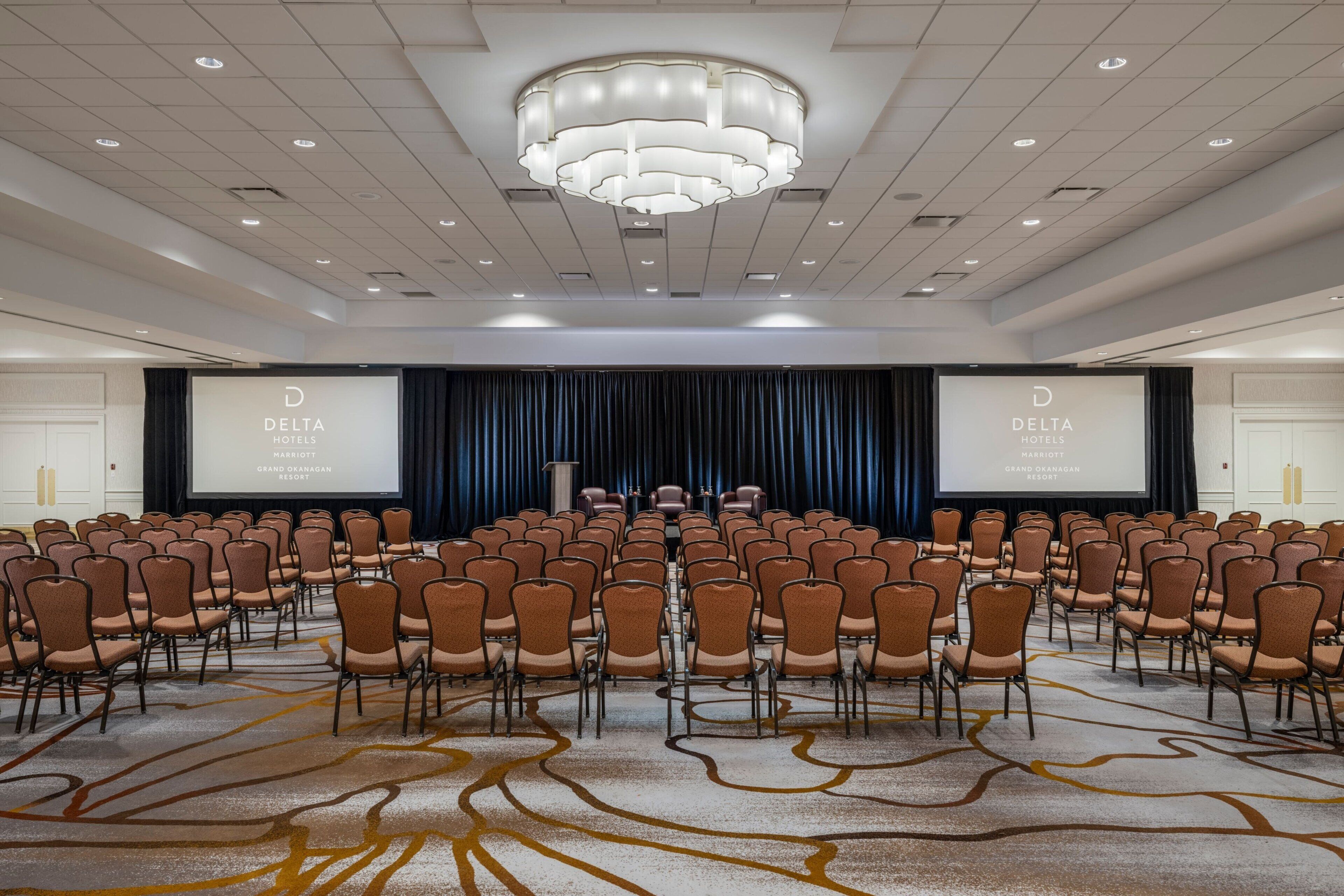 A conference room with rows of chairs, a large screen, and a stage.