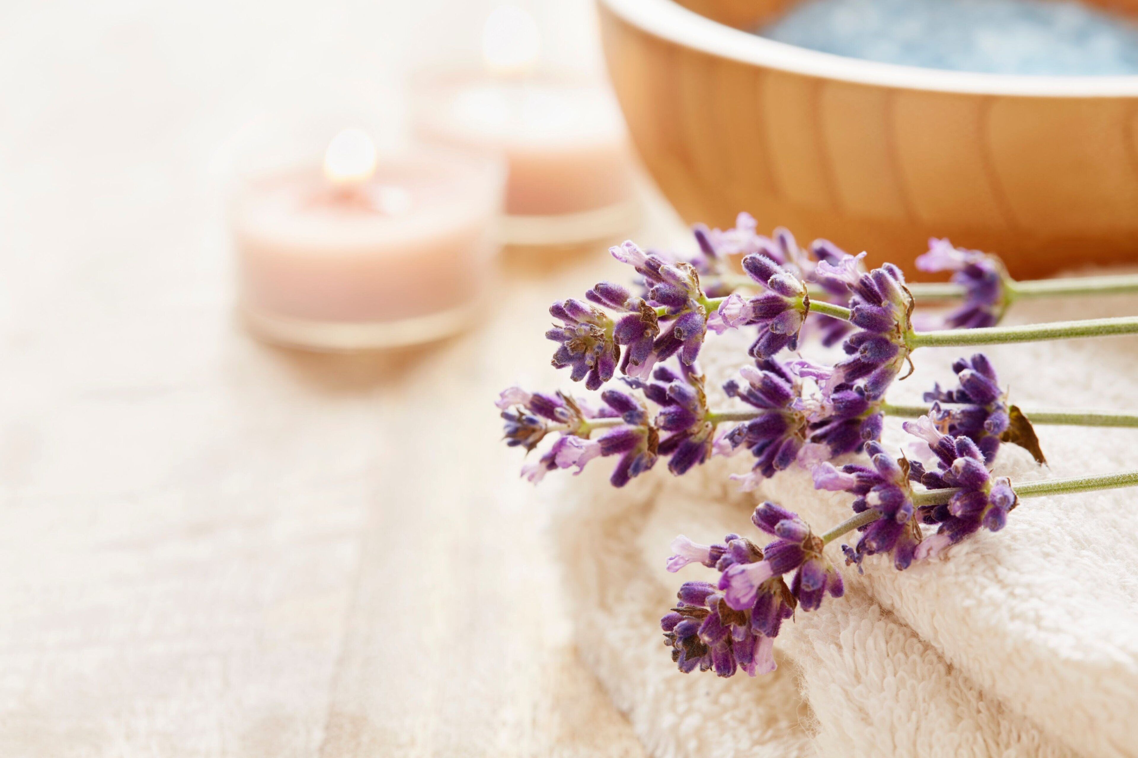 Un entorno de spa con flores de lavanda, velas y un cuenco de madera.