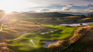 A golf course with a winding path, water hazards, and a distant mountain range. - Delta Hotels by Marriott Grand Okanagan Resort (Kelowna)