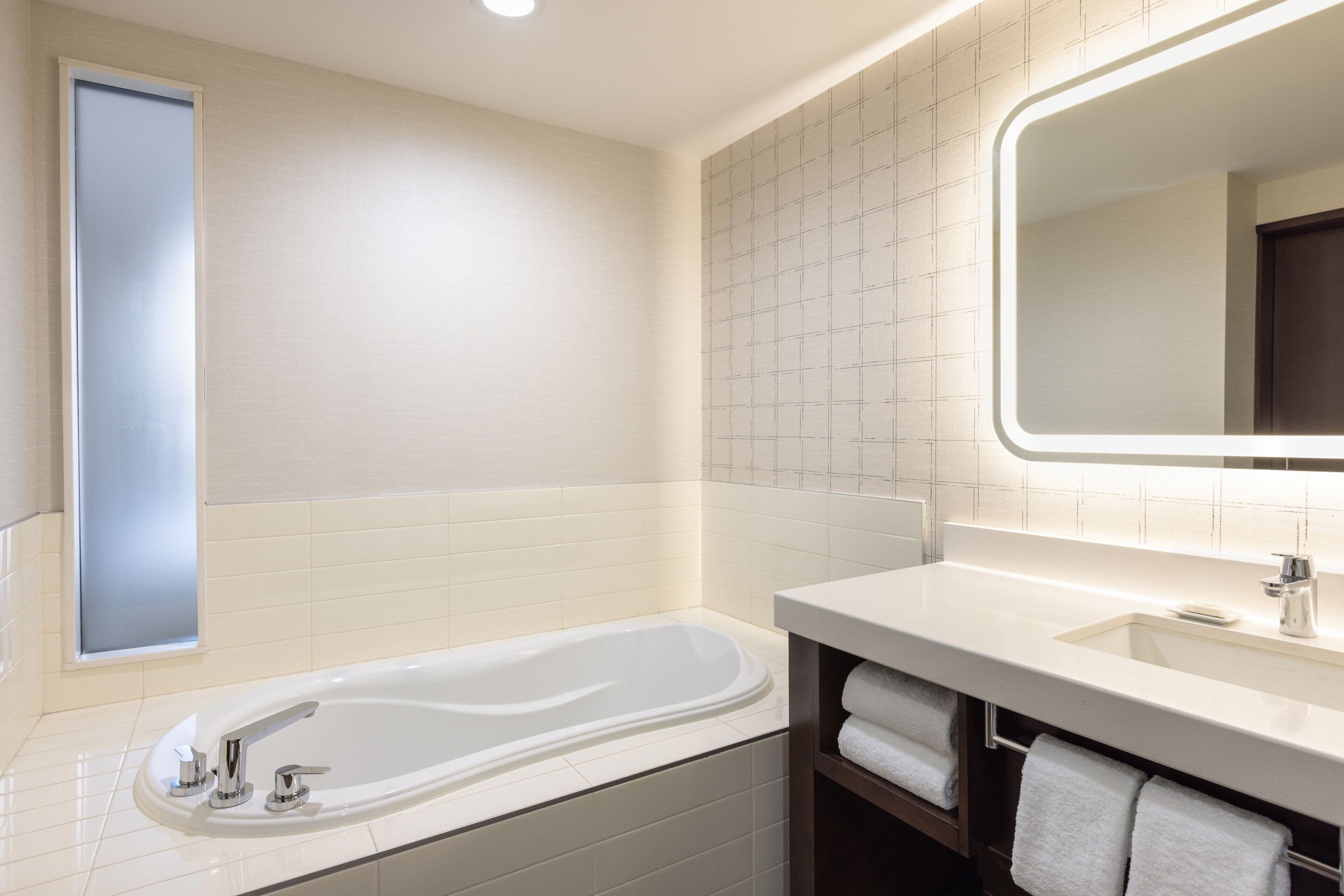 A modern bathroom with a freestanding bathtub, a large mirror, and a vanity with a sink and towel rack.
