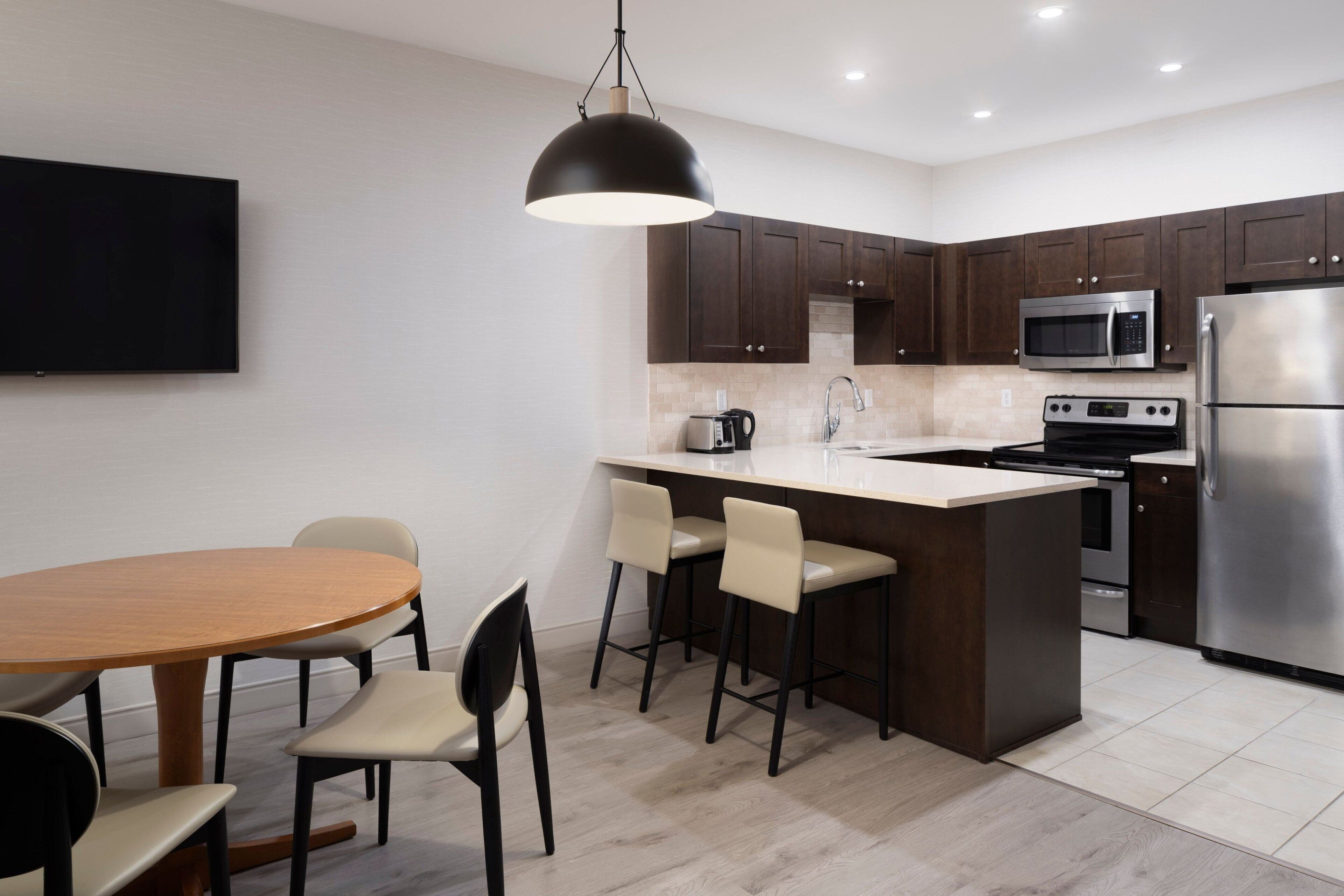 A modern kitchen with dark wooden cabinets, a stainless steel refrigerator, a microwave, and a large island with bar stools.