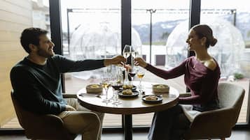 A couple seated at a round table with a view of mountains through a glass enclosure.