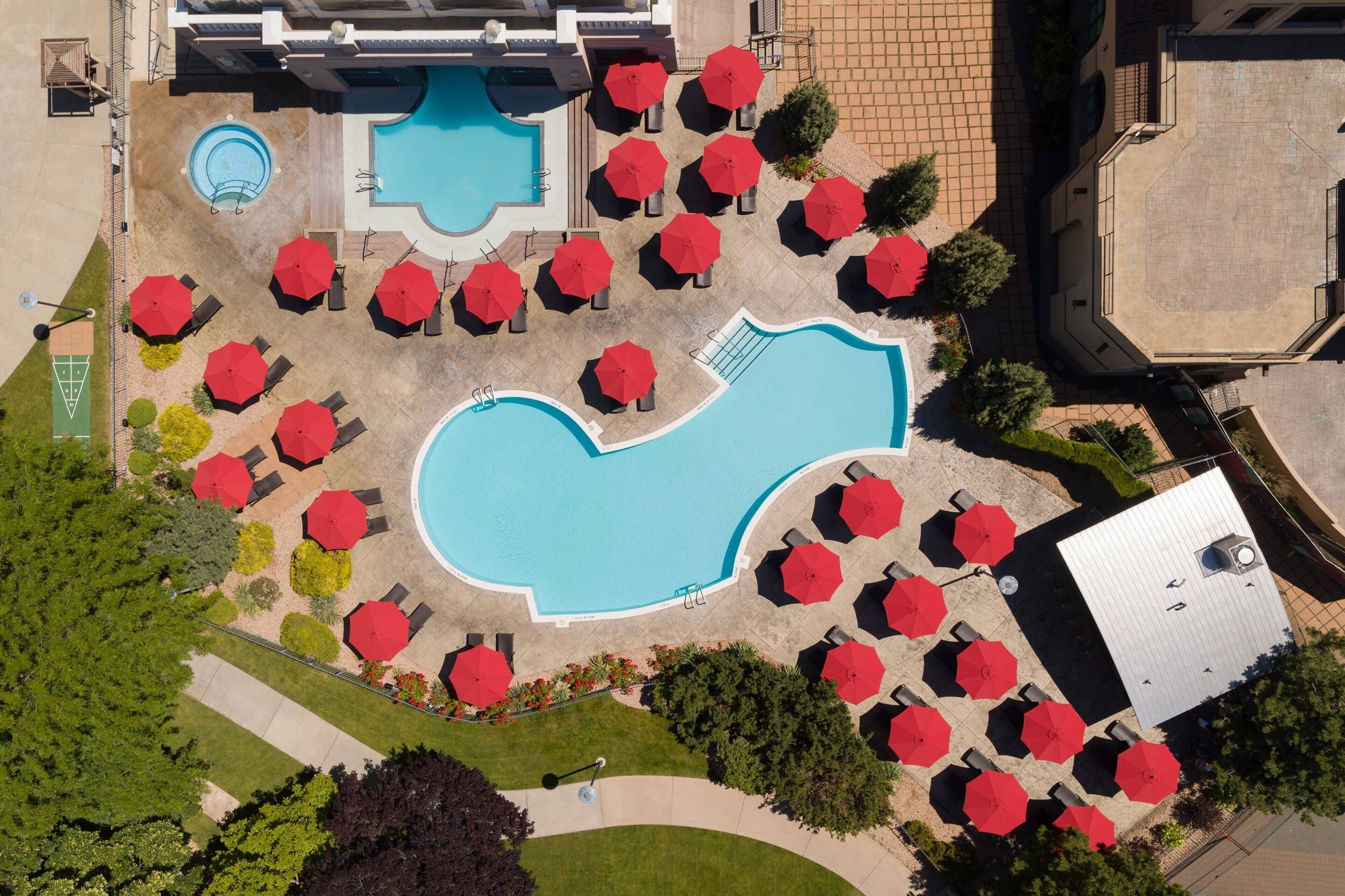 An aerial view of a swimming pool area with multiple red umbrellas and lounge chairs.