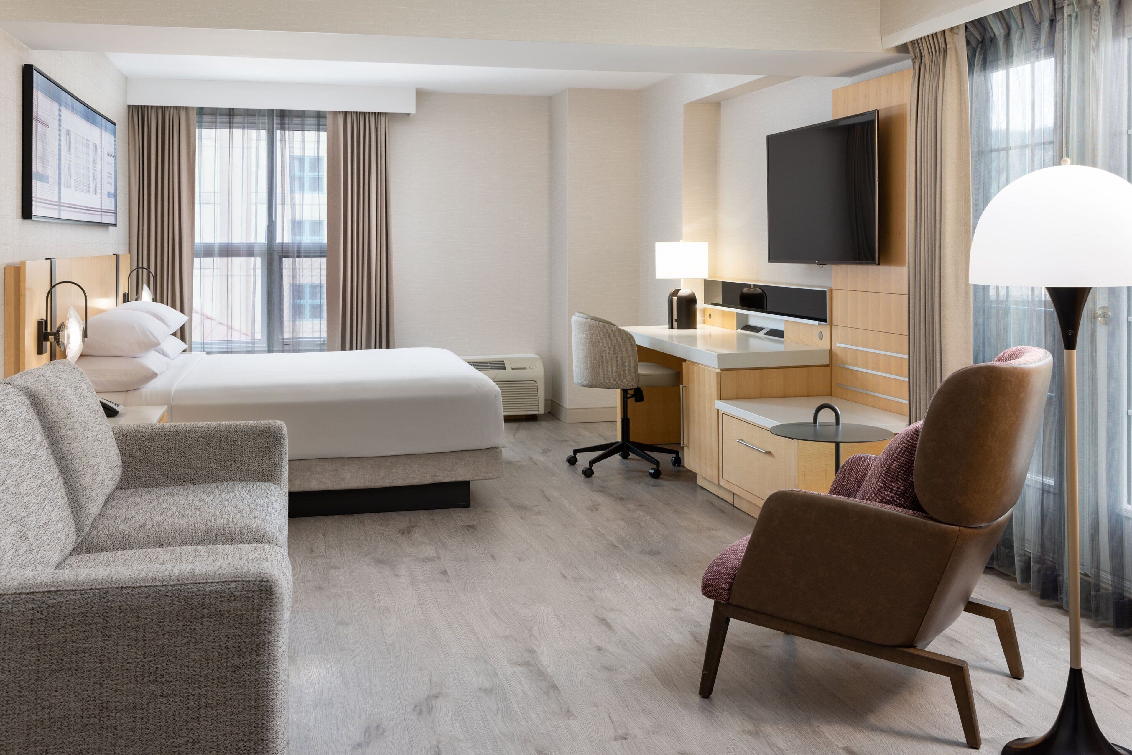 Ett hotellrum med en säng, ett skrivbord, en stol, en tv och en lampa.