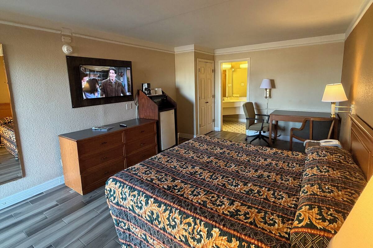 A hotel room with a large bed, a desk, a television, and a bathroom visible through an open door.