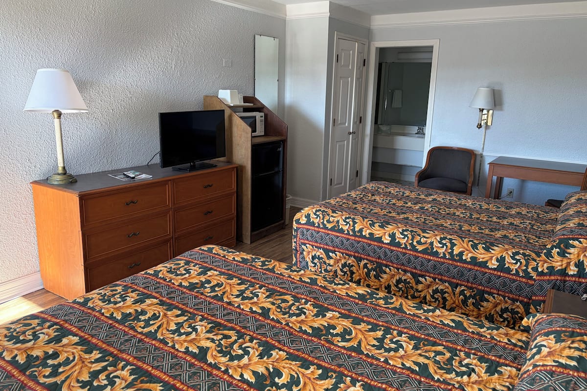 A hotel room with two beds, a dresser, a television, a microwave, and a desk.