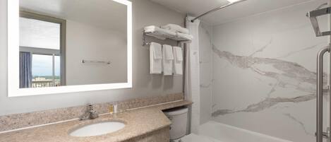 A modern bathroom with a granite countertop sink, a toilet, a bathtub, and a shower.